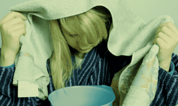 뜨거운 물 그릇에 코 수증기 흡입하는 백인 여성